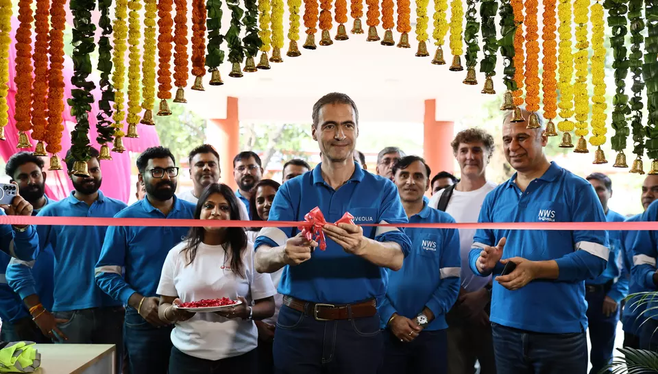 Guillaume Dourdin coupant le ruban inaugural rouge entouré des équipes Veolia sous une arche de guirlandes de fleurs traditionnelles.