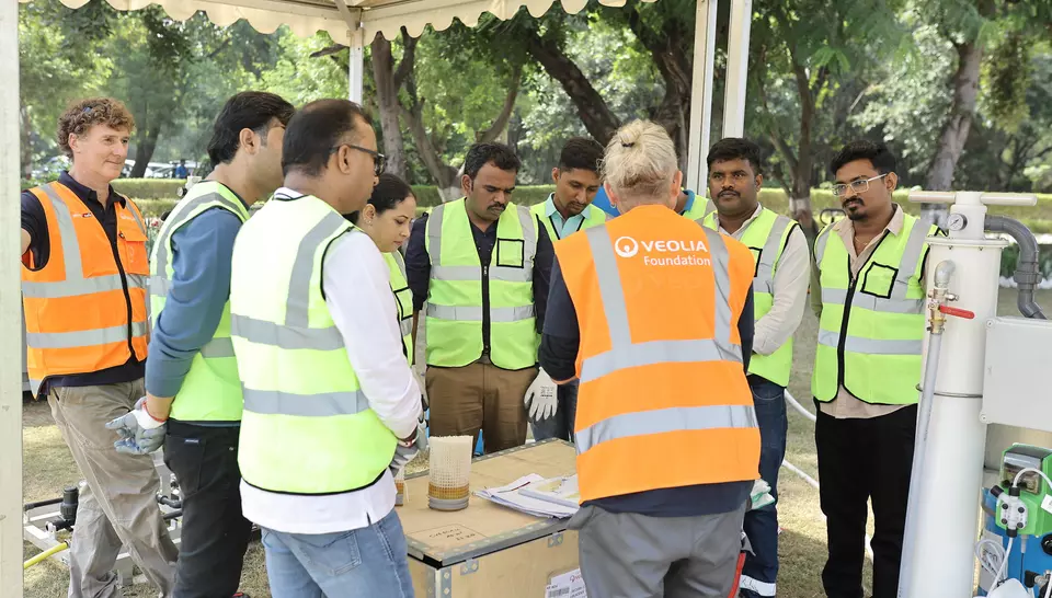 Groupe de collaborateurs en gilets de sécurité écoutant un formateur lors d'un atelier pratique autour d'un équipement de potabilisation de l'eau.